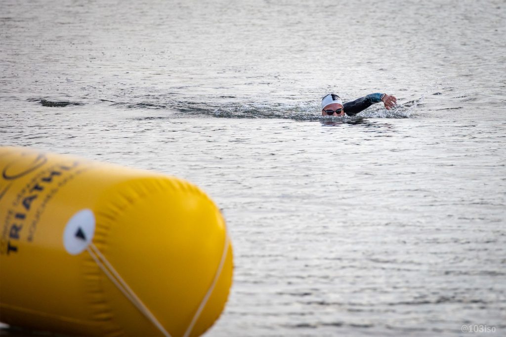 Nageur en eau libre avec bouée de parcours, compétition sportive.