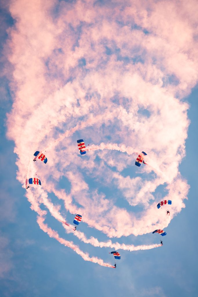 Parachutistes en formation spiralée avec fumigènes colorés.
