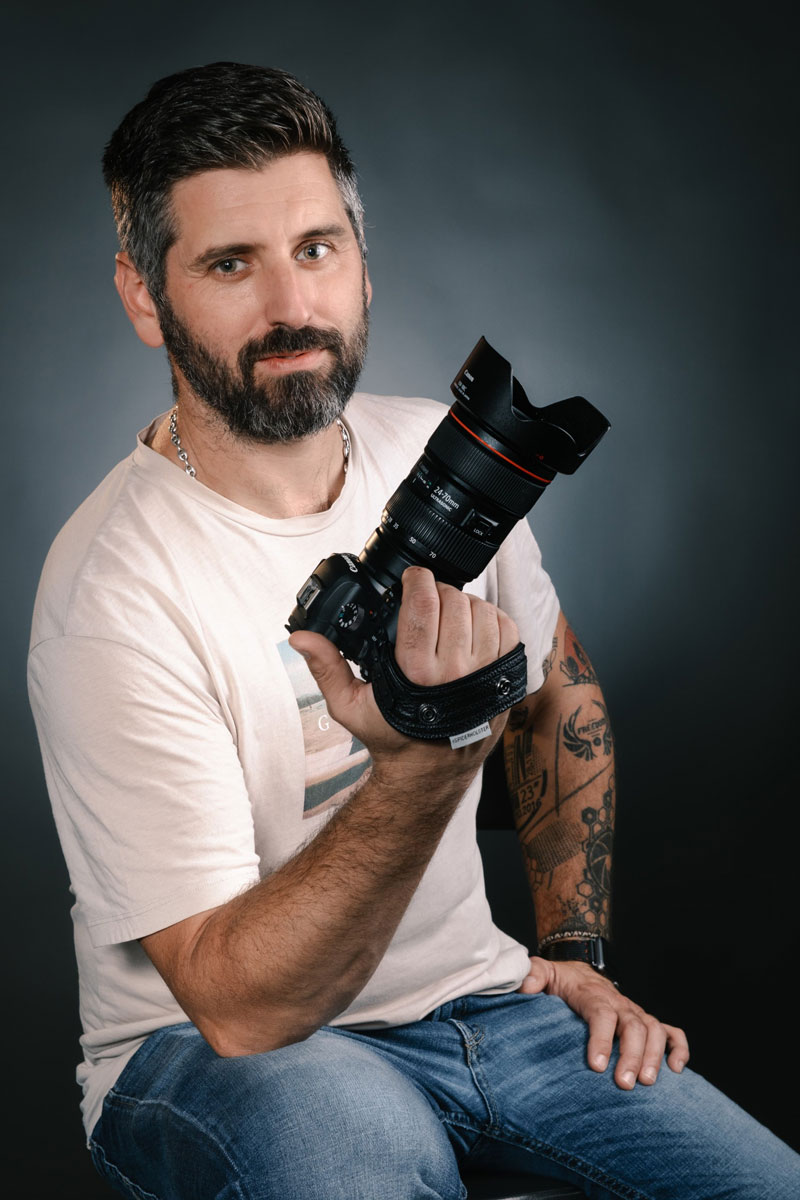 Portrait d’un photographe tenant son appareil photo en studio, lumière douce, style naturel et authentique.