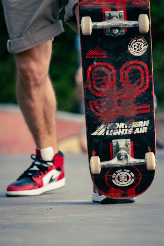 Skateur réalisant une figure en extérieur, focus sur la planche et les jambes.