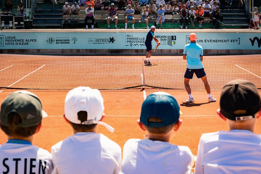 Public d’enfants regardant un match de tennis sur terre battue.