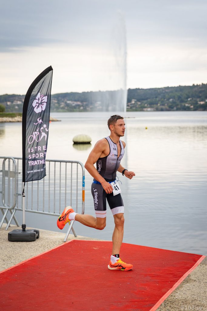 Triathlète courant sur tapis de transition lors d’un événement sportif en extérieur.