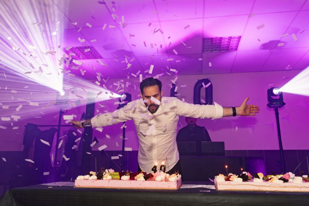 Célébration en intérieur avec confettis, lumière colorée et gâteau d’anniversaire, ambiance festive et joyeuse.
