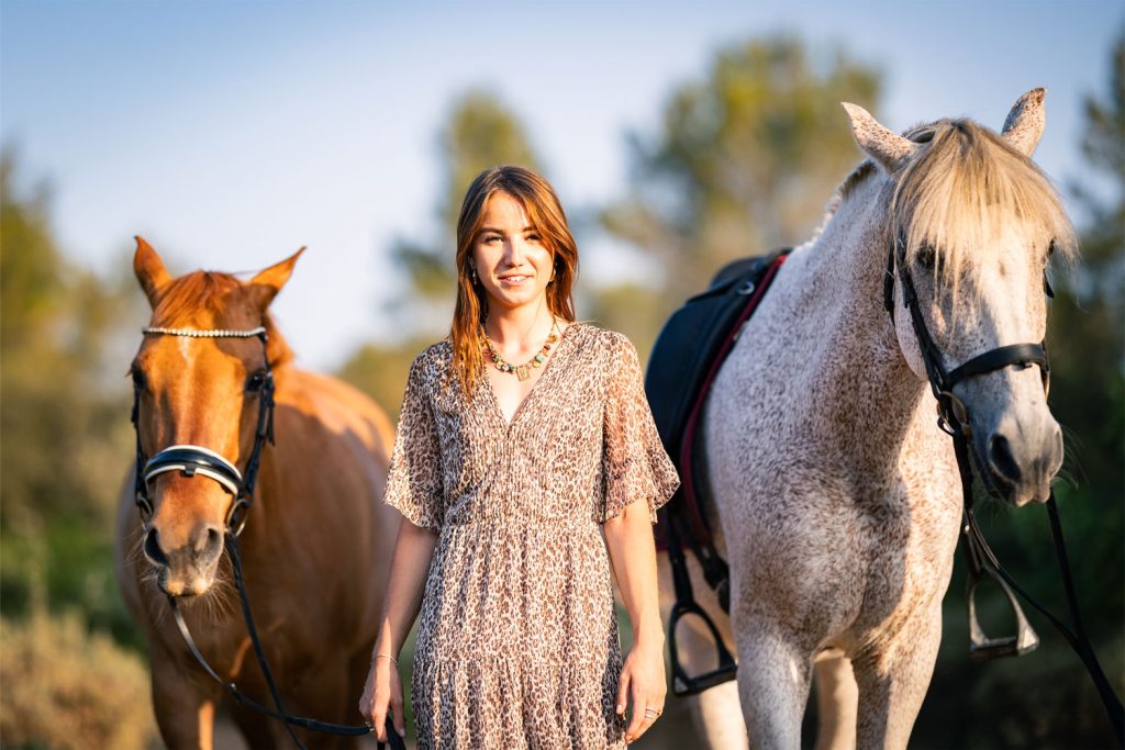 Portrait en extérieur avec deux chevaux, lumière naturelle dorée, ambiance paisible.