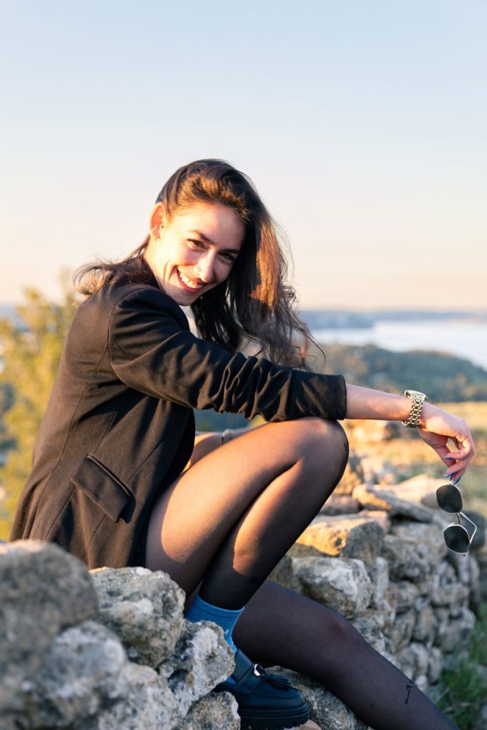Portrait en extérieur au coucher du soleil, modèle assise sur des rochers, ambiance naturelle et lumière dorée.