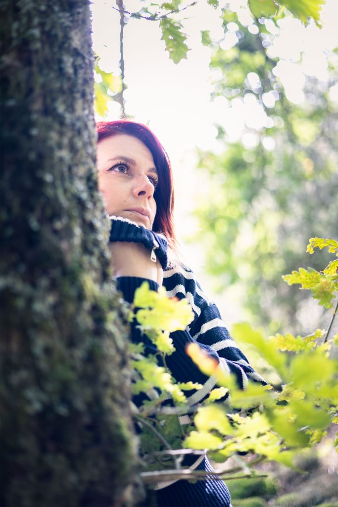Portrait assis contre un arbre, lumière filtrée à travers le feuillage, ambiance contemplative.