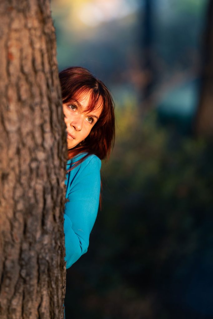 Portrait en extérieur derrière un arbre, lumière douce, regard joueur.